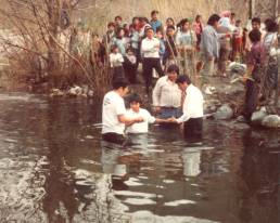 Marcos siendo bautizado en un río junto a otras personas.