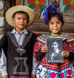 Niños guatemaltecos en traje típico junto al libro Migrante